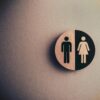 Minimalist gender neutral restroom sign with male and female symbols on textured wall.